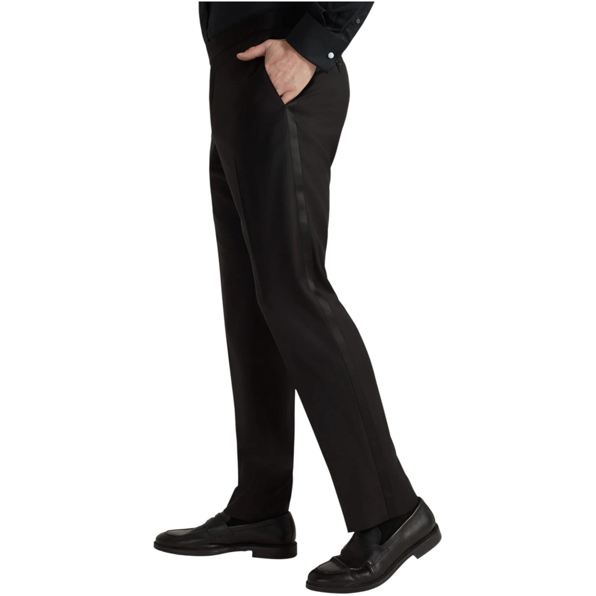 A person wearing the Samuelsohn Bennet Black Honeyway Contemporary Fit Tuxedo, styled with a black shirt and black loafers, stands with one hand in their pocket.