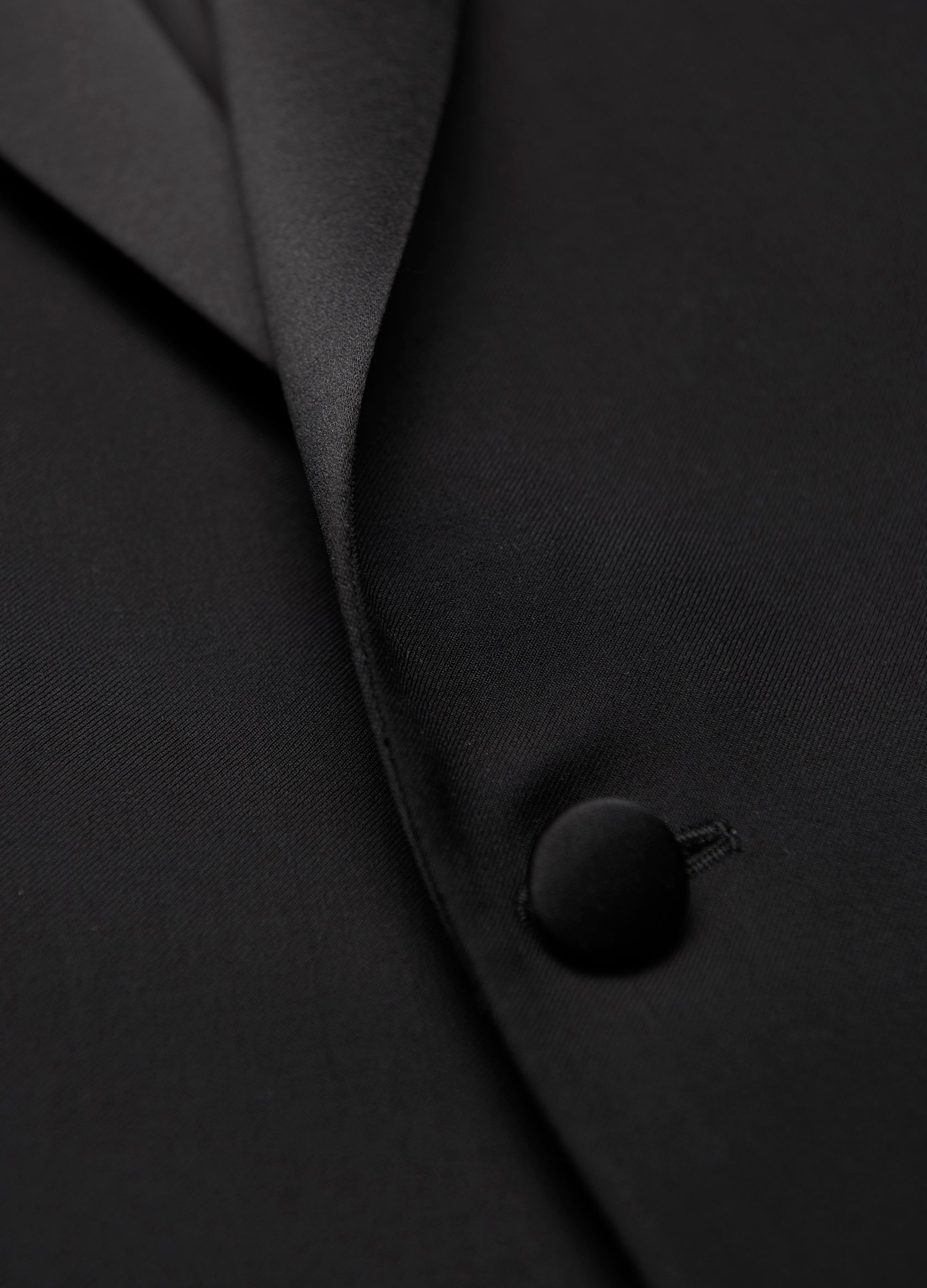 Close-up of a black Samuelsohn Ice Wool fabric with a button, focusing on the texture and fold of the material.