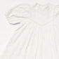 The Early Sunday Girls’ Beth Dress in ivory cotton features a vintage-inspired design with puffed sleeves, a high neckline, lace trim, and delicate floral embroidery. Shown laid flat on a plain white background.