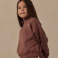 A young girl with long brown hair wears the Rylee & Cru Girls’ Half Zip Sweatshirt in a sporty mauve French terry, paired with matching pants, while standing against a neutral beige background.