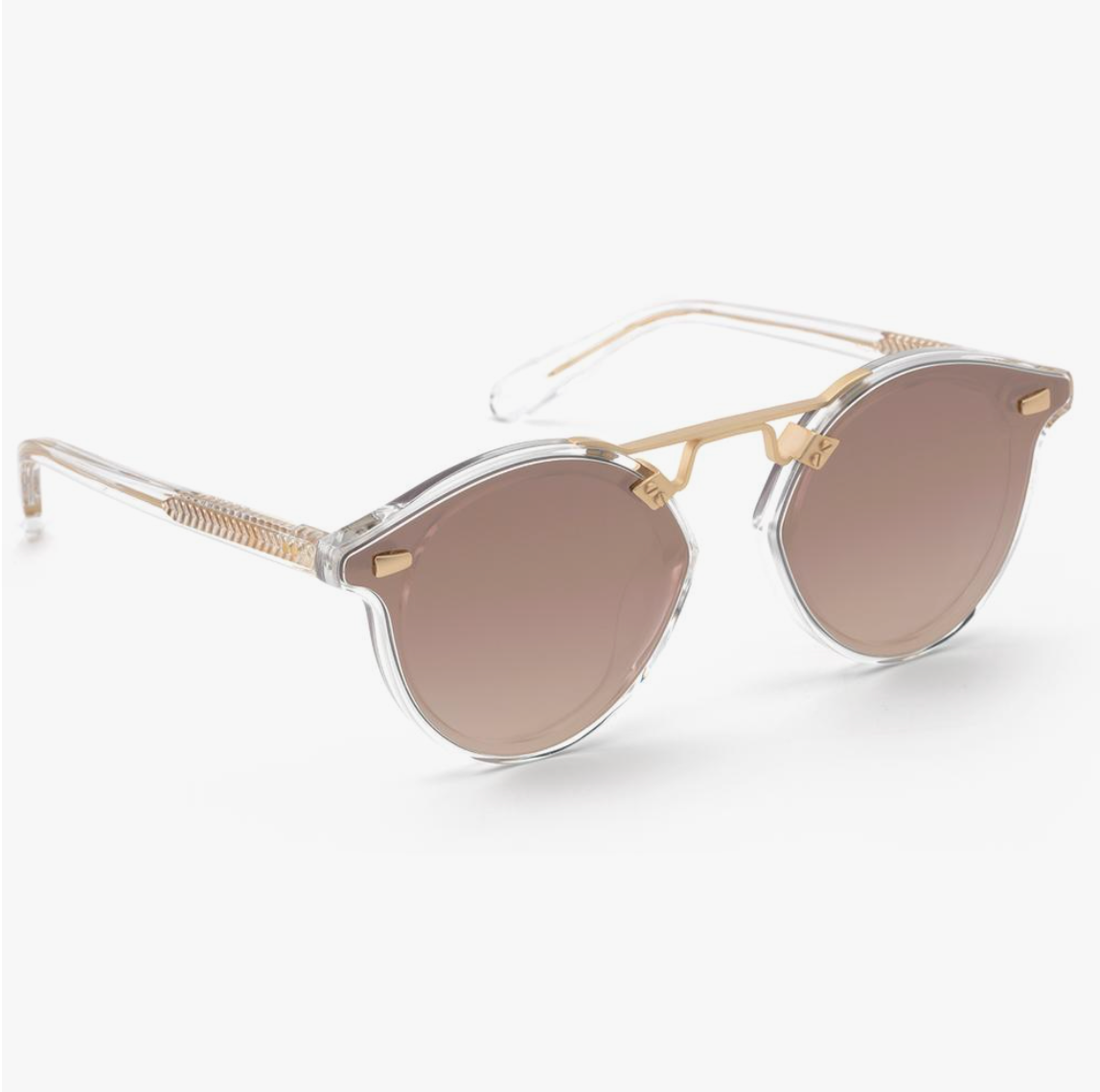 The STL Nylon Sunglasses by Krewe have a clear rim and oversized shape, featuring round brown lenses with gold detailing on the bridge and temples.