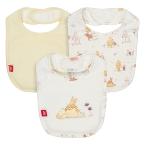 The Magnetic Me Moments With Friends Bib Set includes three eco-friendly TENCEL™ modal bibs: one solid yellow and two white with Winnie the Pooh prints, each featuring neck fasteners and red side tags.