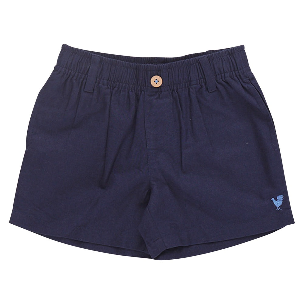 The Boys’ Jackson Short by Pink Chicken features navy blue cotton canvas, an elastic waistband, button closure, belt loops, and a small embroidered rooster on the left leg.