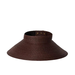 The Birdie Visor by Janessa Leone is a wide-brimmed brown raffia straw visor with an open top and adjustable back strap, shown on a plain white background.