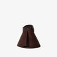 The Janessa Leone Birdie Visor is a brown woven lampshade with a flared conical shape, reminiscent of raffia straw, and features a dark leather accent and metal rivets near the top.