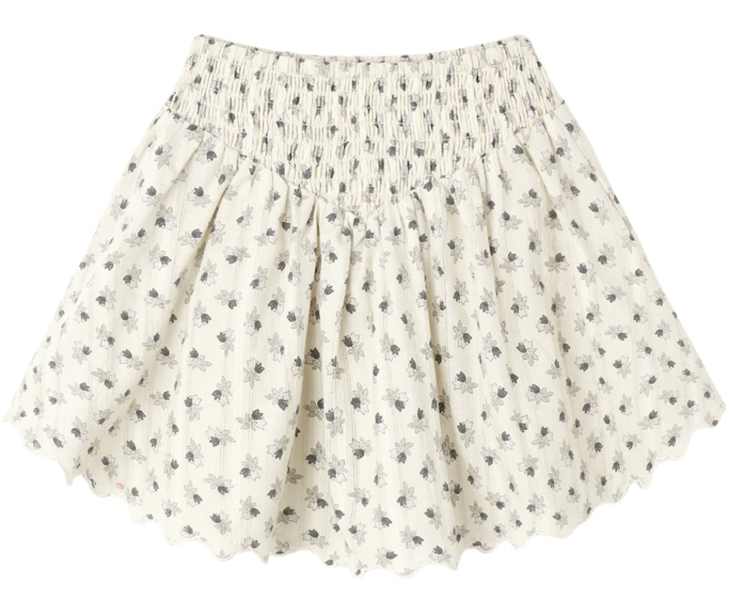 The Girls’ Smocked V Mini Skirt by Rylee & Cru features a smocked waistband, scalloped hem, and a delicate small black floral print on lightweight fabric. This timeless silhouette effortlessly blends comfort and style for an elegant look.