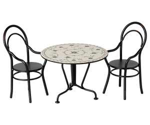 The Maileg MAIL Dining Table Set includes a small round table with a decorative white top and two matching black metal chairs with curved backs, all in miniature size.