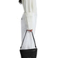 A person stands in profile, dressed in a white ribbed sweater, white pants, and white shoes, holding a small black Proenza Schouler Bond Smooth Nappa Bag with supple leather and shoulder to crossbody function down by their side.