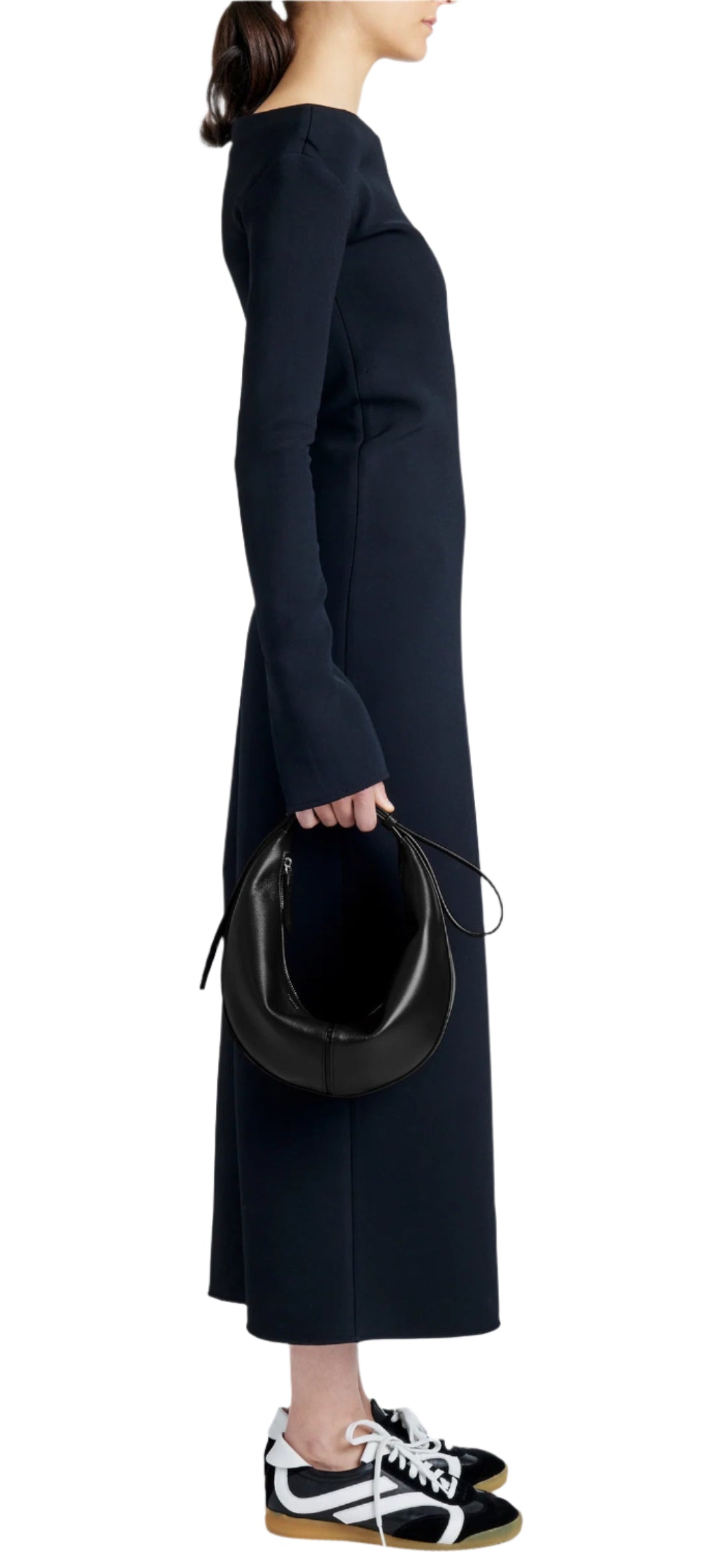 A person in a long, dark dress and sneakers is holding a Proenza Schouler Slide Bag crafted from supple leather, viewed from the side.