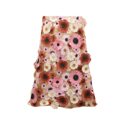 The Blooming Meadow Skirt by Dorothee Schumacher is an A-line midi skirt with a pink mesh overlay decorated with couture-inspired 3D floral appliqués in shades of pink, red, white, and beige.