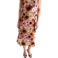 Model wearing the Blooming Meadow Skirt by Dorothee Schumacher, featuring a colorful floral pattern and delicate 3D embroidery, stands with arms relaxed and feet in black sandals against a white background.