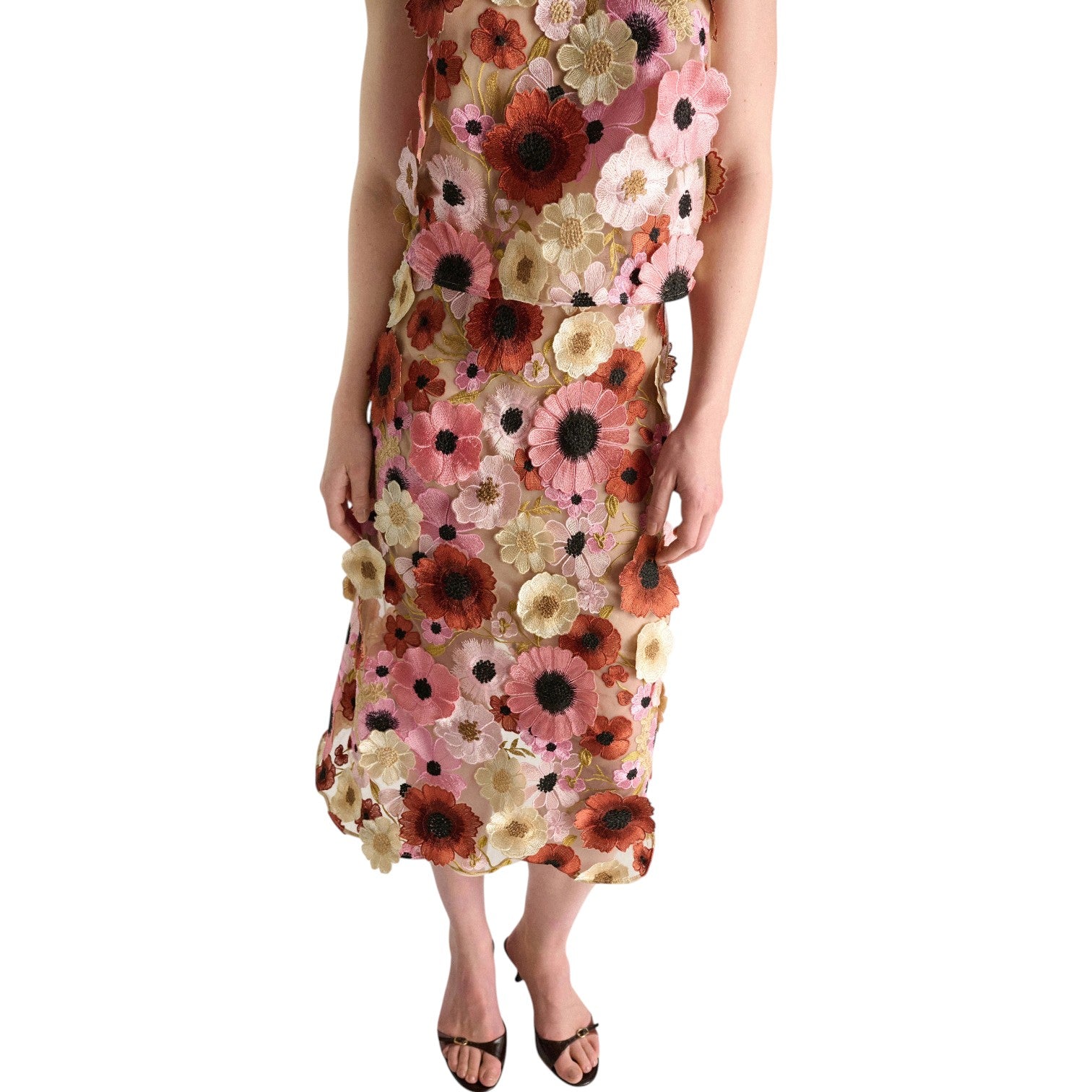 Model wearing the Blooming Meadow Skirt by Dorothee Schumacher, featuring a colorful floral pattern and delicate 3D embroidery, stands with arms relaxed and feet in black sandals against a white background.
