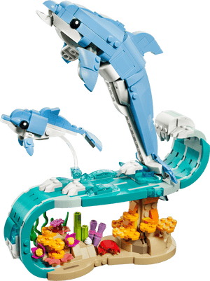 Two LEGO® sea animal figures—a large and a small dolphin—leap over a wave above a coral reef, all built with the Legos - Toyhouse LEGO® Creator 3-in-1 Sea Animals: Beautiful Dolphins set.