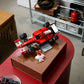 The LEGO® Icons Ferrari F2004 & Michael Schumacher set by Legos - Toyhouse features a model car and minifigure displayed on a brown box in a modern room with shelves and furniture.