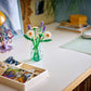 A tidy desk with a yellow lamp, a jar of Legos - Toyhouse LEGO® Botanicals Daisies artificial flowers, a white organizer tray, stacked books, and a folded cloth on a green mat.