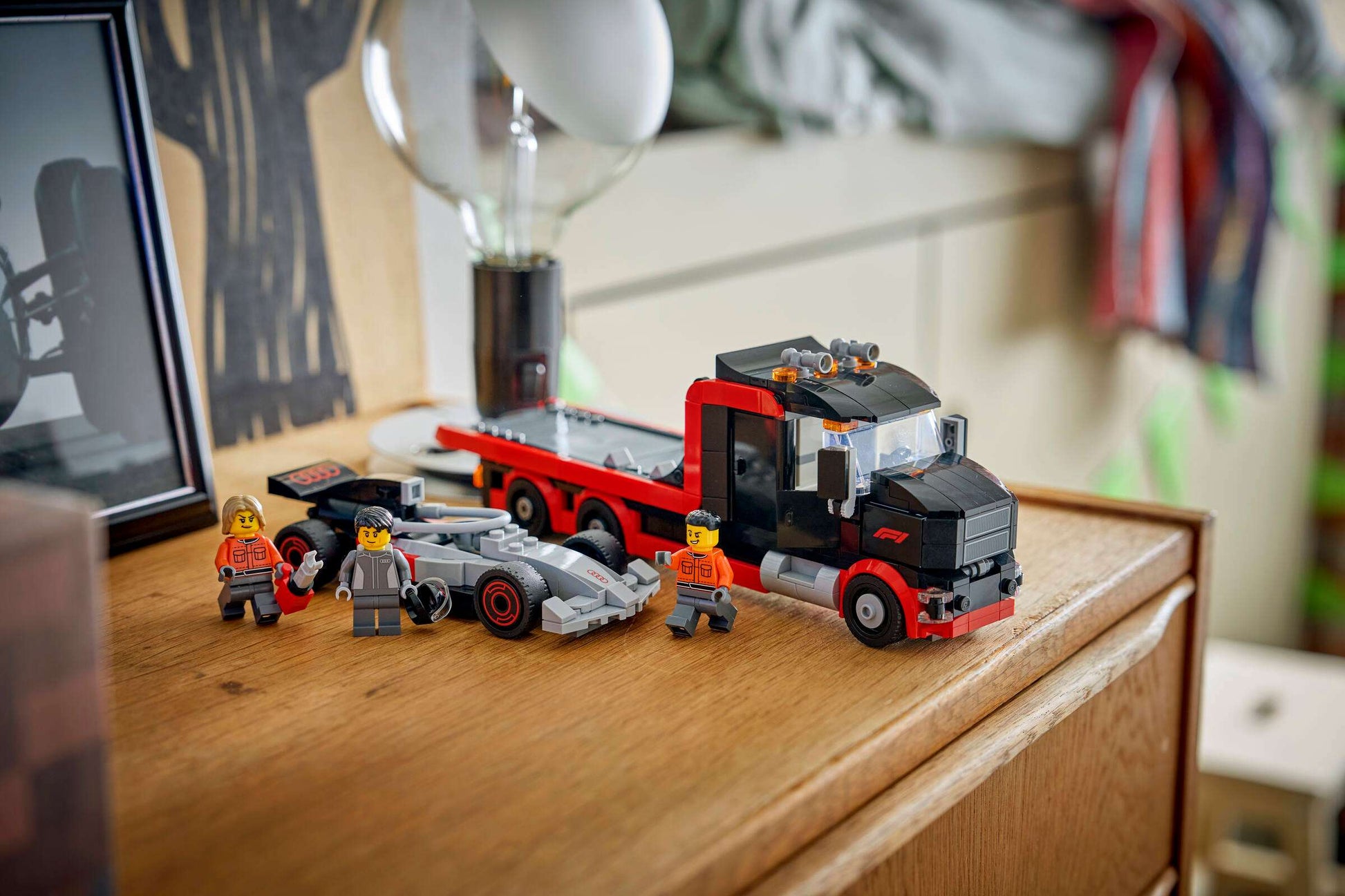 A LEGO® City F1® Display Truck with Audi F1® Race Car by Legos - Toyhouse and three minifigures are arranged on a dresser beside a lamp, photo, and more—ideal for displaying your toy car building kit.
