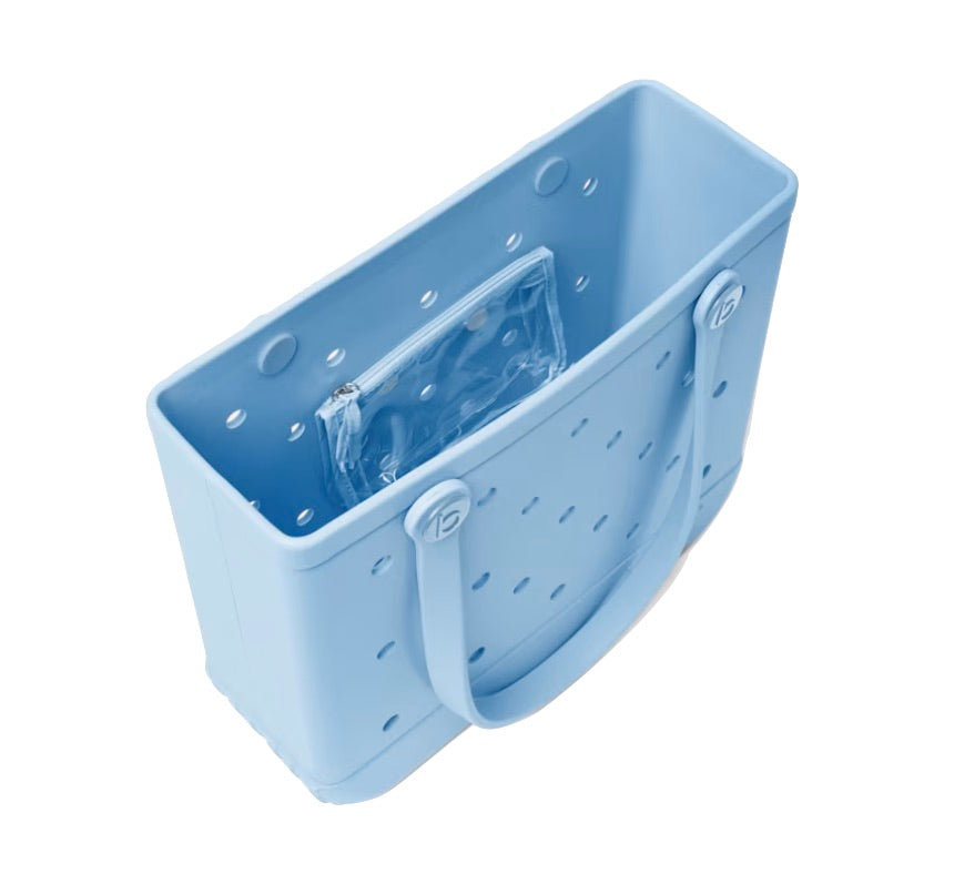 The Baby Bogg® Bag by Bogg Bags features a light blue rectangular design with circular and diamond-shaped holes, double handles, and a transparent zippered pouch inside. This durable tote is also washable, making it ideal for everyday use.