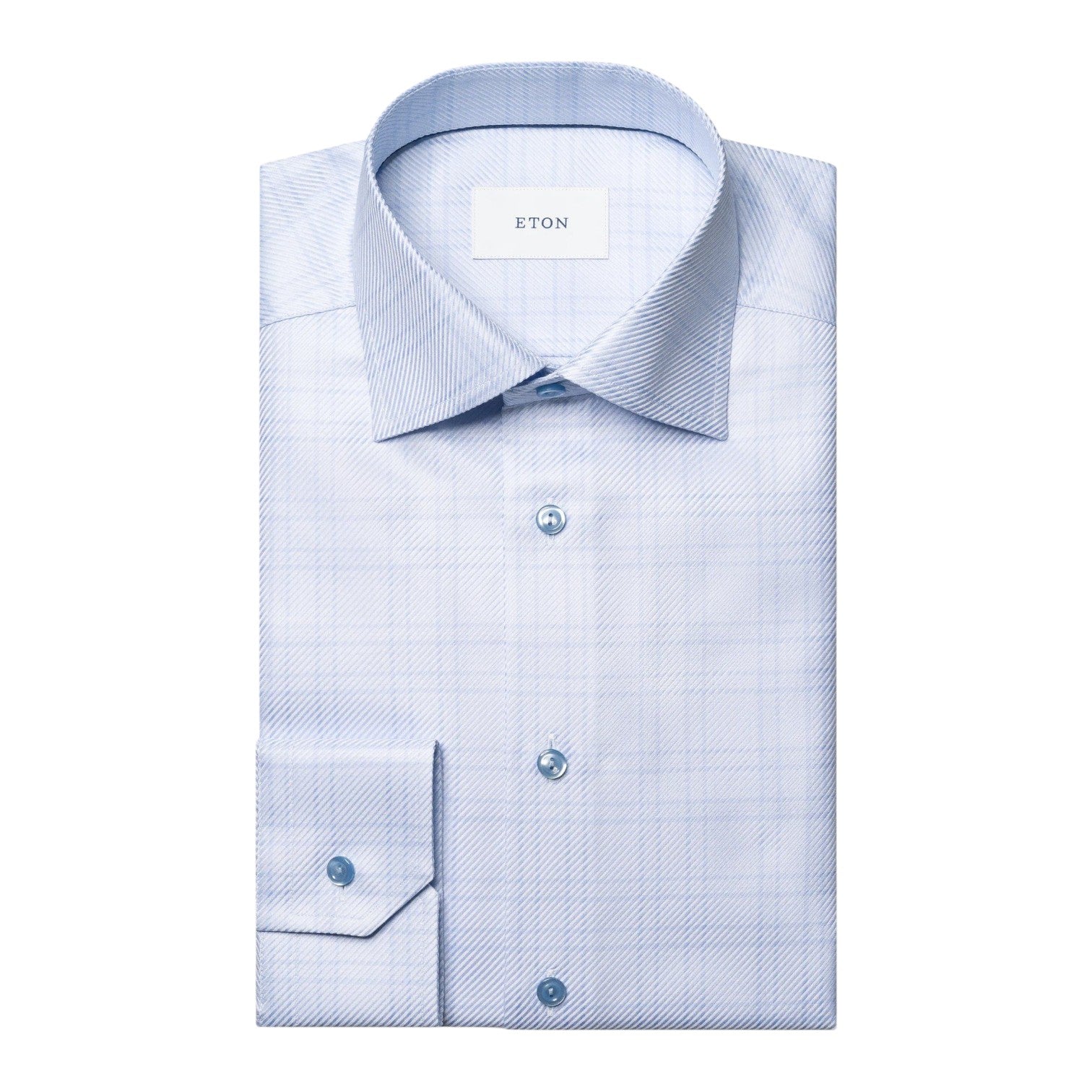 The Eton King Check Twill Shirt is a light blue, plaid-patterned dress shirt with a spread collar and buttoned cuffs, crafted from organic cotton. Neatly folded, it’s displayed on a white background.