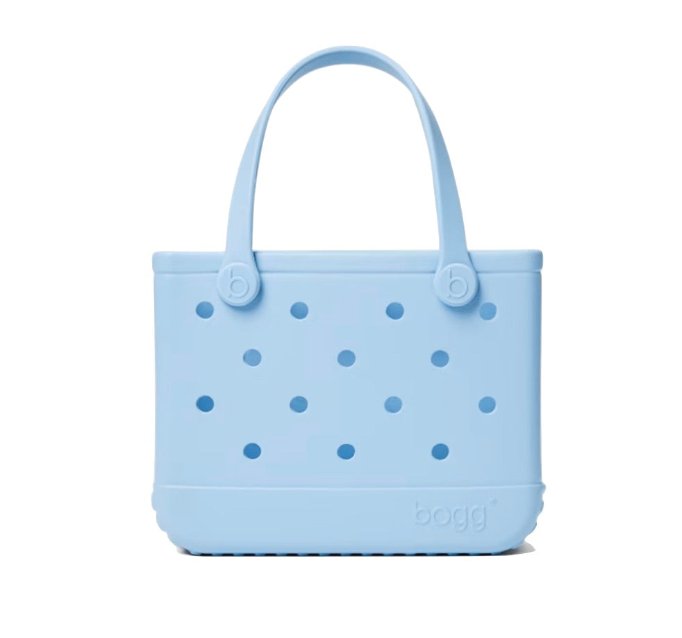Light blue, rectangular Bitty Bogg® Bag tote from Bogg Bags featuring round cutout holes, sturdy handles, and “bogg” embossed at the bottom right. This compact and washable bag is perfect for everyday use.