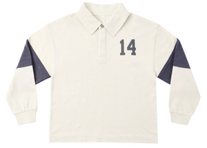 The Rylee & Cru Baby Boys’ and Boys’ Rugby Polo features long sleeves, a cream color, a classic collar with buttoned neckline, navy “14” on the chest, and navy panels on the upper sleeves for a timeless athletic look.