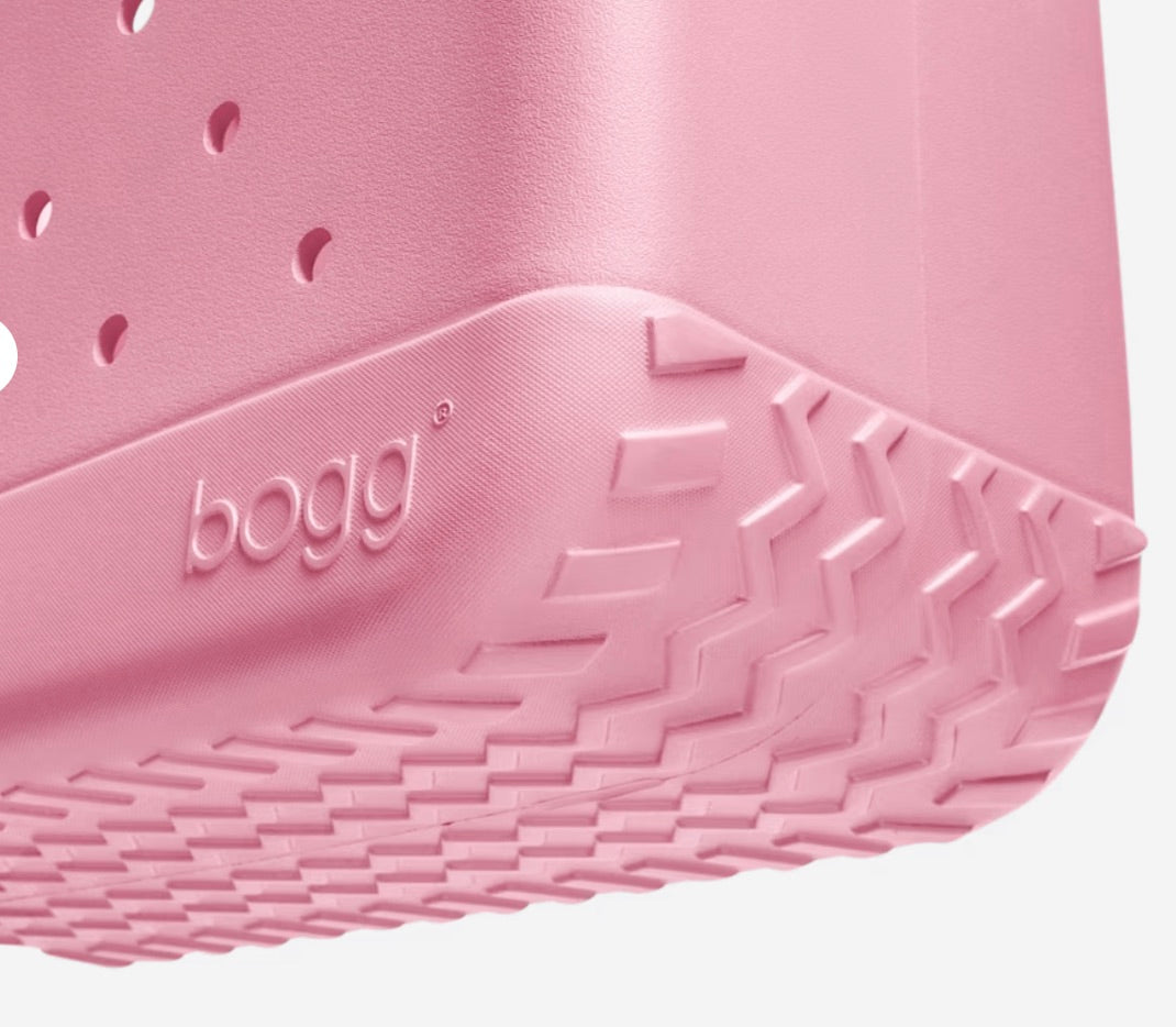 Close-up of a pink Original Bogg® Bag by Bogg Bags, showcasing its textured bottom corner with the raised “bogg” logo and distinctive grooved tread pattern. This washable bag combines style and practicality for everyday use.