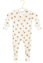 The Baby Teddy Zipper Footie by Lou Lou & Company is a cozy, cream-colored onesie with foot coverings, featuring an all-over brown bear face print. Crafted from silky-soft fabric, it is displayed on a gold hanger.