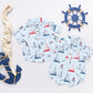 Two Baby Boys' Easton Jumpers from Pink Chicken in light blue with nautical prints are shown beside a decorative rope, anchor, and ship wheel on a white background.