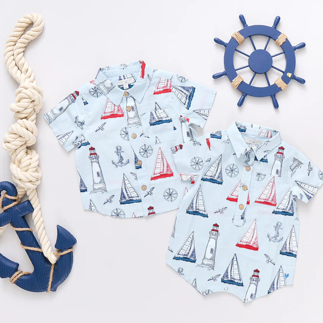 Two Baby Boys' Easton Jumpers from Pink Chicken in light blue with nautical prints are shown beside a decorative rope, anchor, and ship wheel on a white background.