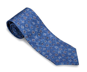 The R. Hanauer Brinkley Medallion Necktie by R. Hanauer is a 3 1/4 inch silk necktie, made in the USA, featuring a rolled-up blue design adorned with a geometric pattern of small squares and rectangles in contrasting colors.