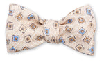 Hand-made in Fort Mill, the R. Hanauer Brinkley Medallion Bowtie is a beige silk accessory adorned with a sophisticated geometric pattern of blue and brown squares.