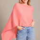 Wearing the Alashan Cashmere Dress Topper Poncho in light pink with blue jeans, a person stands against a neutral background, one hand in their pocket—showcasing this essential cashmere style.