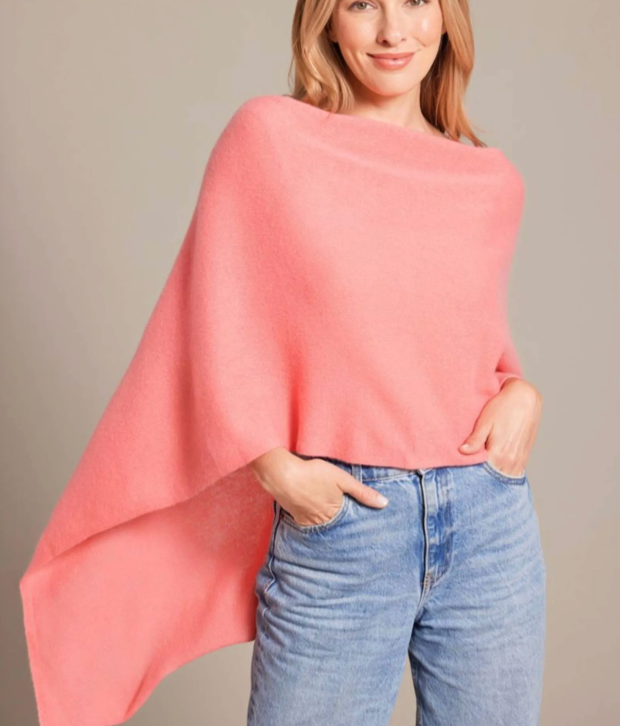 Wearing the Alashan Cashmere Dress Topper Poncho in light pink with blue jeans, a person stands against a neutral background, one hand in their pocket—showcasing this essential cashmere style.