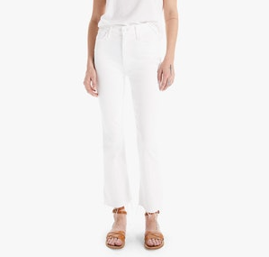 A person stands against a plain backdrop, effortlessly stylish in a white t-shirt and Mother's The Hustler Ankle Fray high-waisted white denim with frayed hems, complemented by chic tan sandals.