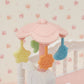 A Calico Critters Crib with Mobile featuring a pink crib mobile adorned with yellow star, orange flower, and blue bird-shaped hanging toys, displayed above a white crib against a floral wallpaper background—ideal for completing your whimsical baby nursery set or pairing with other Calico Critters dollhouse furniture.