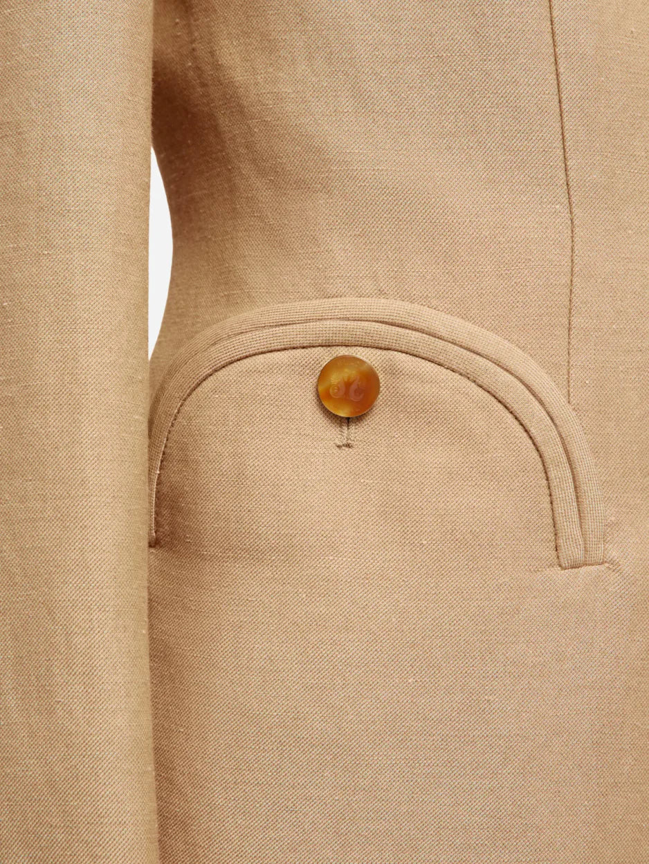 Close-up of the Renegade Charmer Blazer by Blaze Milano, featuring beige linen and a rounded pocket with a single brown button.