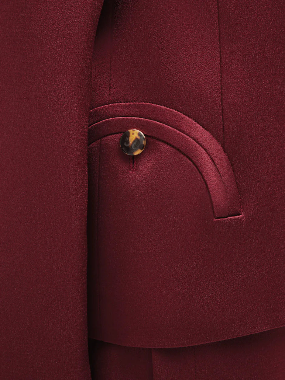 Close-up of a maroon Novalis Sunfire Blazer pocket by Blaze Milano, featuring a brown marbled button and curved stitching detail.
