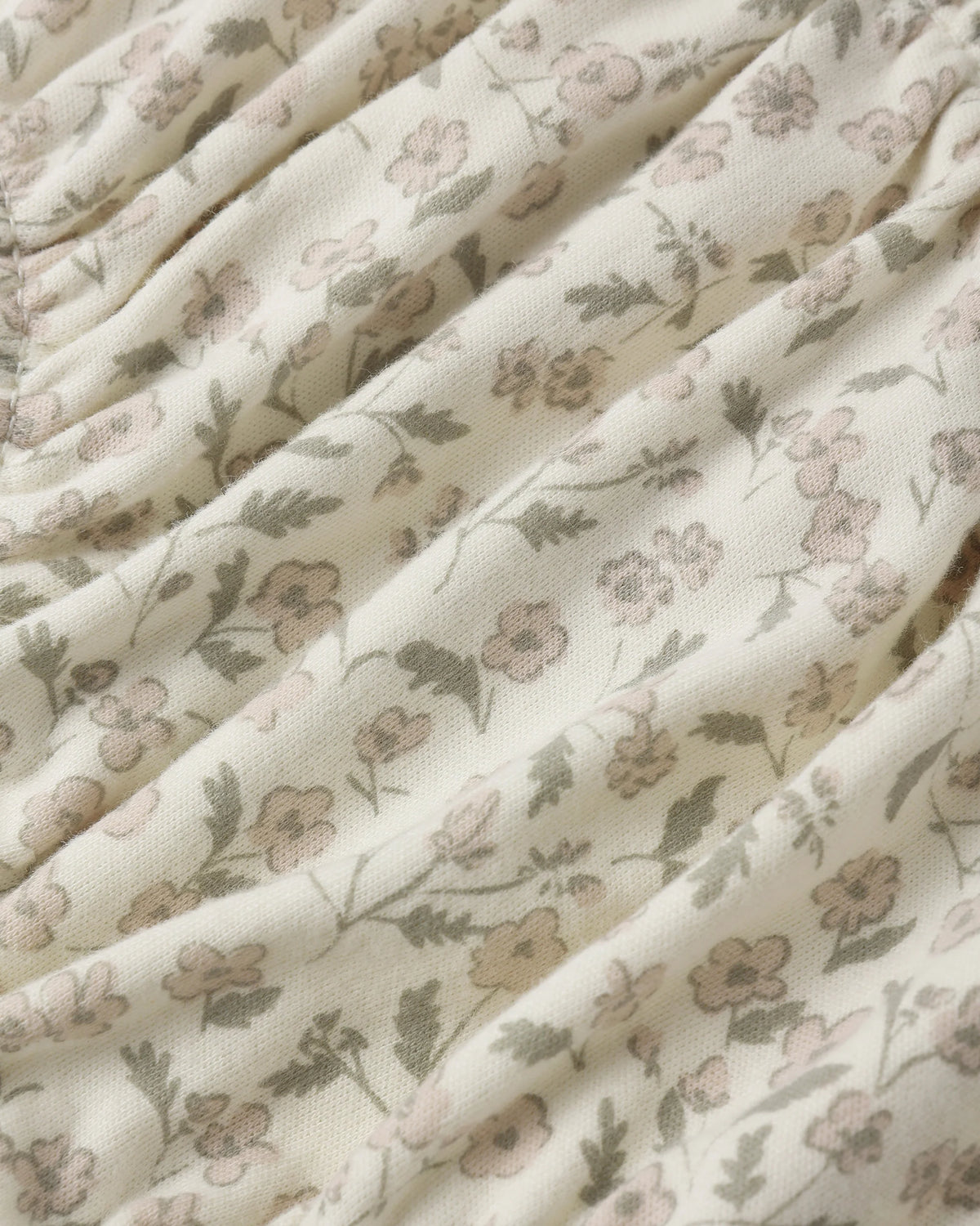 Close-up of the Quincy Mae Baby Girls’ Gathered Bloomer, crafted from cream-colored fabric with a gathered texture and adorned with a delicate small floral print in muted pink, green, and beige—perfectly designed with elasticated leg openings for adorable comfort.