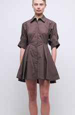 A model wears the Simkhai Jazzie Mini Dress, a brown collared, button-down cotton poplin dress with short sleeves and a flared skirt, set against a plain light background.