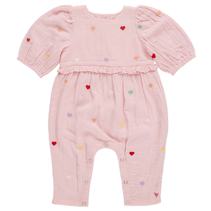 The Pink Chicken Baby Girls' Brooke Jumper features candy heart embroidery on a pink romper with puff sleeves, multicolored heart patterns, and waist ruffle detailing, designed for easy diaper changes.