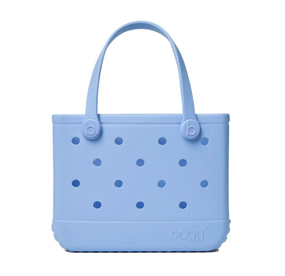 The Bitty Bogg® Bag by Bogg Bags is a compact, light blue tote featuring round holes on the sides and two sturdy handles. Crafted from a flexible, rubber-like material, this washable bag is both stylish and easy to clean.