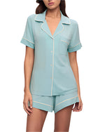 Someone dressed in the Eberjey Gisele Relaxed Short PJ Set: light blue short-sleeved pajamas with white trim, a buttoned shirt with a functional pocket, and matching shorts for comfort.