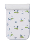 The Kissy Kissy Golf Championship Burp Cloth is crafted from white Pima cotton and features blue and green golf-themed prints—carts, clubs, flags, balls—and a charming blue scalloped trim.