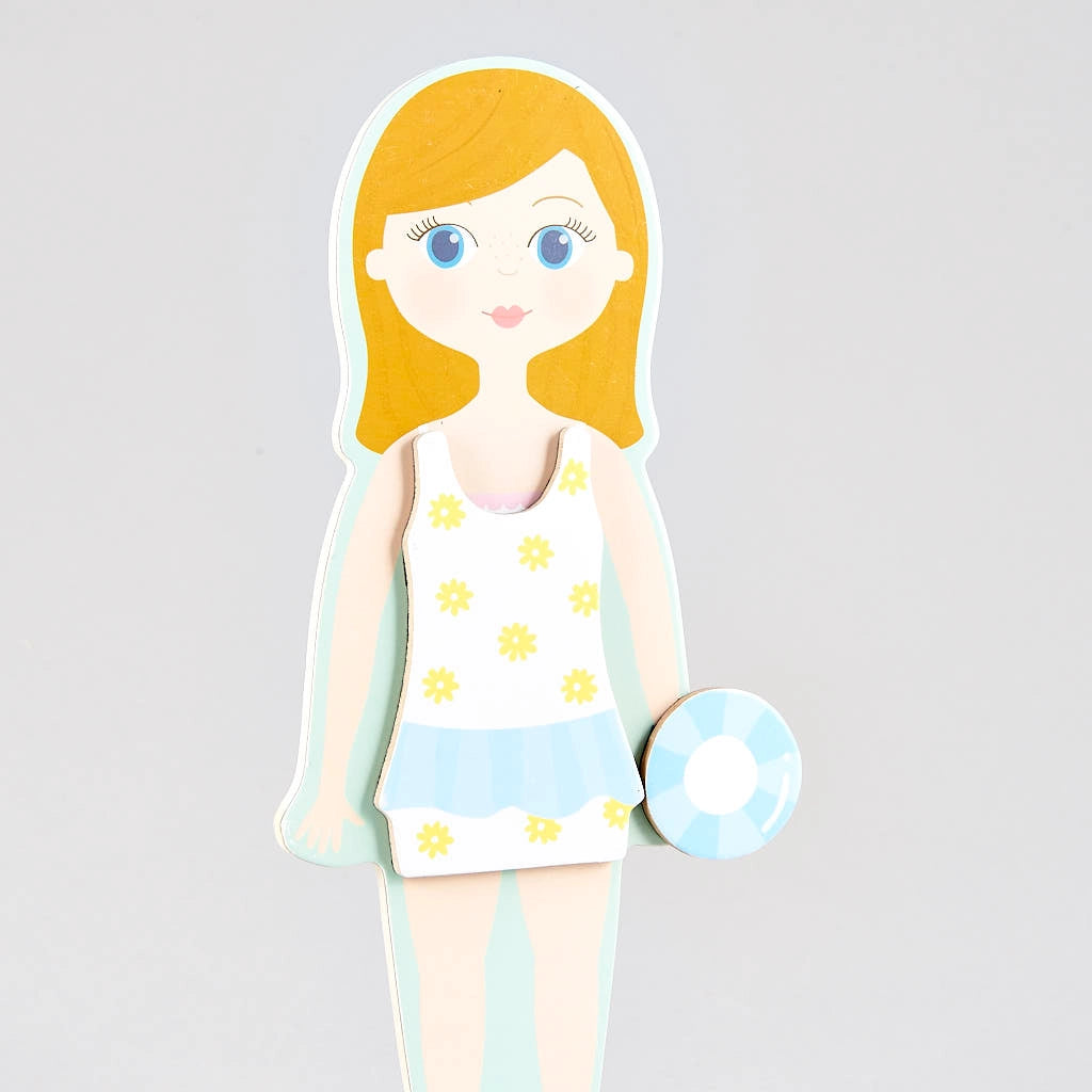 Illustration of the Elsie Magnetic Dress Up Character by Floss and Rock—a girl with blonde hair in a white and yellow floral swimsuit, holding a blue and white float, standing against a plain gray background—reminiscent of a magnetic dress up doll ready to showcase her summer style.