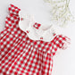 The Kidiwi Baby Girls' Charlotte Romper features red and white gingham with a white scalloped collar and embroidered cherries, shown alongside baby's breath flowers on a white background.