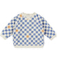 The Arsene & Les Pipelettes Baby Sweatshirt is made from soft organic fleece and features a cream base with a blue checkerboard pattern, accented by scattered orange squares and finished with a classic crew neckline.