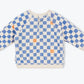 The Arsene & Les Pipelettes Baby Sweatshirt is a long-sleeve top made from soft organic cotton fleece, featuring a blue and orange checkered pattern on a cream background and shown laid flat on a plain light surface.