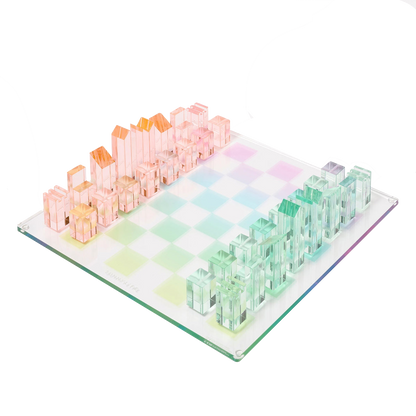 The Sunnylife Lucite Chess and Checkers, Aurora set by Sunnylife showcases a retro style with transparent pink and green pieces arranged on a pastel checkered board, exuding a kaleidoscopic color charm.