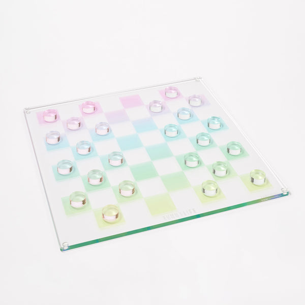 The Sunnylife Lucite Chess and Checkers, Aurora board displays a pastel checkered pattern against a glass surface, featuring transparent round pieces that create a kaleidoscopic color scheme reminiscent of a classic Lucite game set.