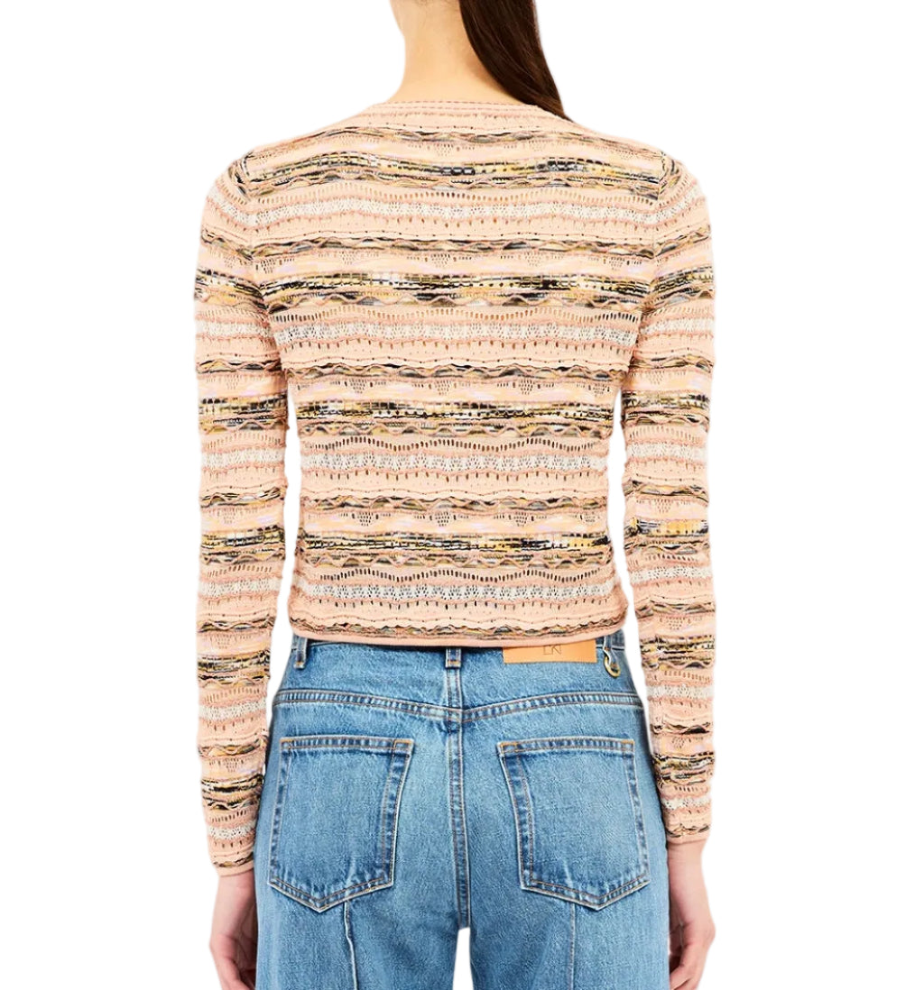 A woman stands facing away, wearing the Ulla Johnson Mia Knit Cardigan in pink and beige with blue high-waisted jeans.