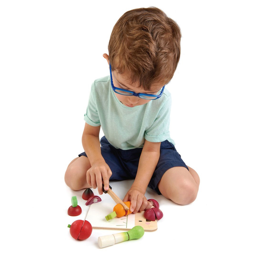 Young boy with glasses playing with a Tenderleaf Mini Chef Chopping Board from Tender Leaf Toys on a white background.